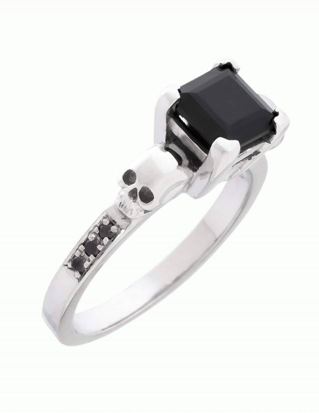 Thyone is a women's gothic ring with skulls and black diamonds. A robust setting holds the square cut gemstone in the center. Below the skulls, the ring is set with three diamonds on each side. View from diagonally above.
