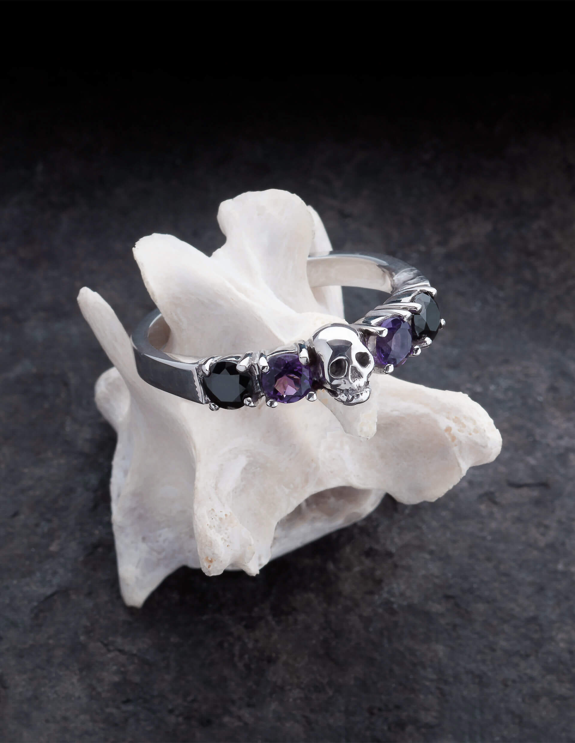 Helice ist ein prachtvoller Ehering mit einem Totenkopf umgeben von vier runden Edelsteinen. Der Ring ist aus Silber gefertigt in der Goldschmiede Kipkalinka. Der Ring liegt auf einem Knochen.
