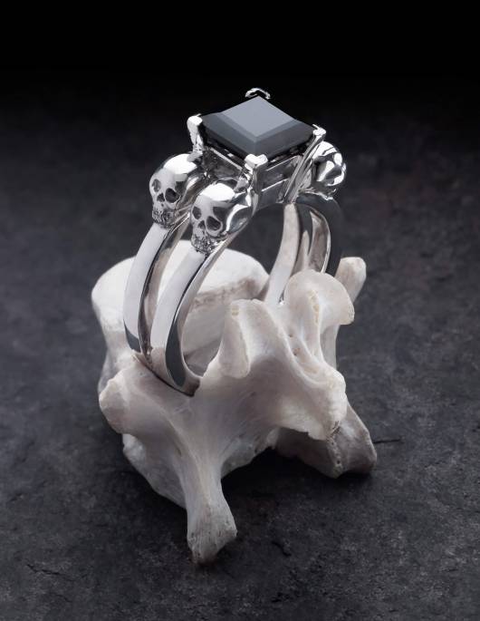 Lethe is a women's skull ring in silver. A black, angular gemstone sits in the centre. Shown on a bone.            