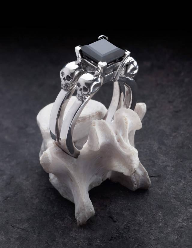 Lethe is a women's skull ring in silver. A black, angular gemstone sits in the centre. Shown on a bone.            