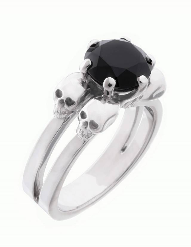 Lilith est une bague noble à tête de mort pour les femmes gothiques. La bague sobre est fabriquée en argent et porte une pierre précieuse noire au centre entre quatre petites têtes de mort. Vue oblique du haut.