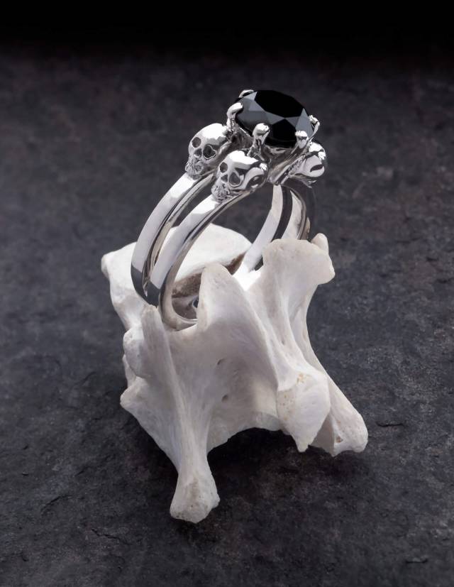 Lilith es un anillo de calavera noble para mujeres góticas. El sencillo anillo es de plata y tiene una gema negra en el centro entre cuatro pequeñas calaveras. Se muestra de pie sobre un hueso.