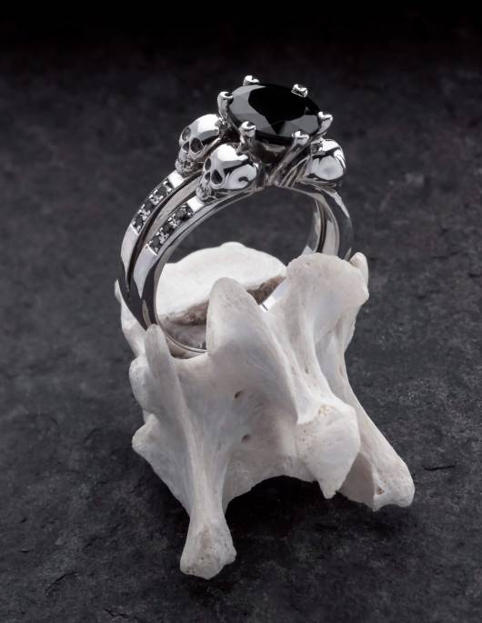 Lilith es un elegante anillo de calavera con diamantes negros y una gema negra redonda. El anillo está hecho de plata y es el anillo de compromiso gótico perfecto. El anillo está colocado sobre un hueso.