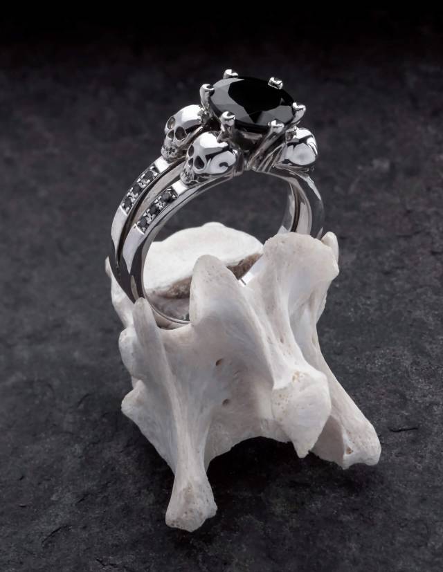 Lilith is an elegant skull ring with black diamonds and a round black gemstone. The ring is made of silver and is the perfect gothic engagement ring. The ring is draped on a bone.