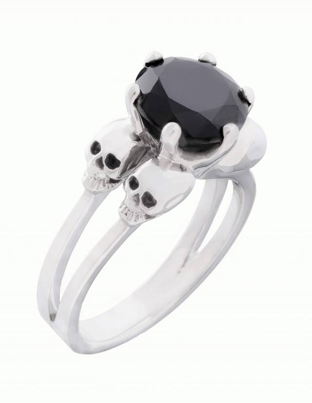 Varla is an engagement ring with small skulls made of silver. Between the four skulls sits a large, round gemstone. View diagonally from above.