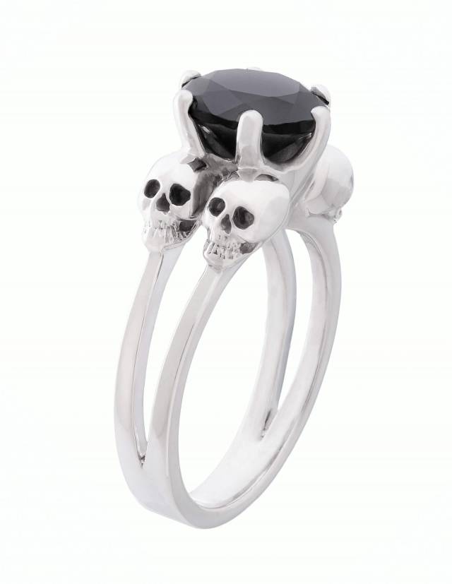 Varla is an engagement ring with small skulls made of silver. A large round gemstone sits between the four skulls. Side view.