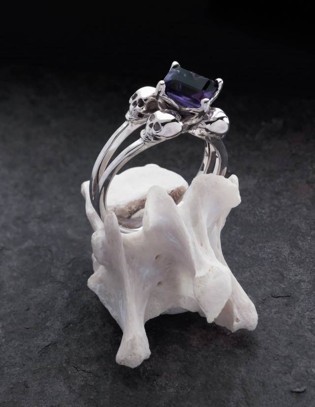 A silver skull ring with an angular purple gemstone for women