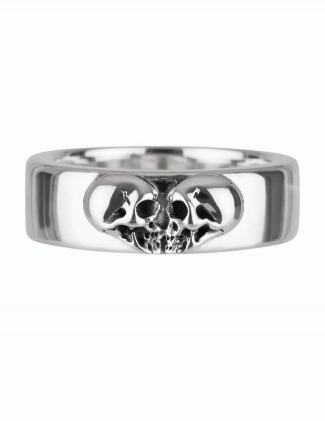 Kissing Skulls è un anello in argento massiccio in stile gotico. Due teschi di profilo sono disposti a forma di cuore. La forma dell'anello è ampia e leggermente piatta a cupola con bordi arrotondati. Mostrato direttamente dal davanti.