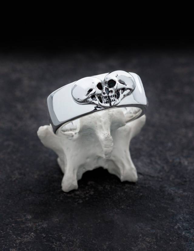 <div>Kissing Skulls is a heavy gothic wedding ring. Two skulls in profile are shaped in the form of a heart. The shape of the ring is wide and slightly curved with rounded edges. The ring is shown on a bone.</div>