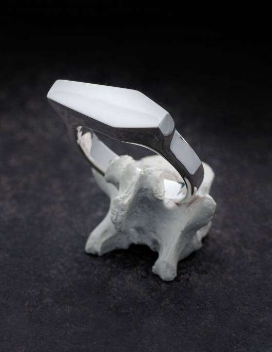 Necromance ist ein großer Siegelring in Form eines Sarges. Die Oberfläche des Ringes aus 925er Silber ist glatt und glänzend. Die Kanten der Ringschiene sind angenehm gerundet. Das Design ist massiv, schlicht und elegant. Der Ring wird hier auf einem Knochen gezeigt.