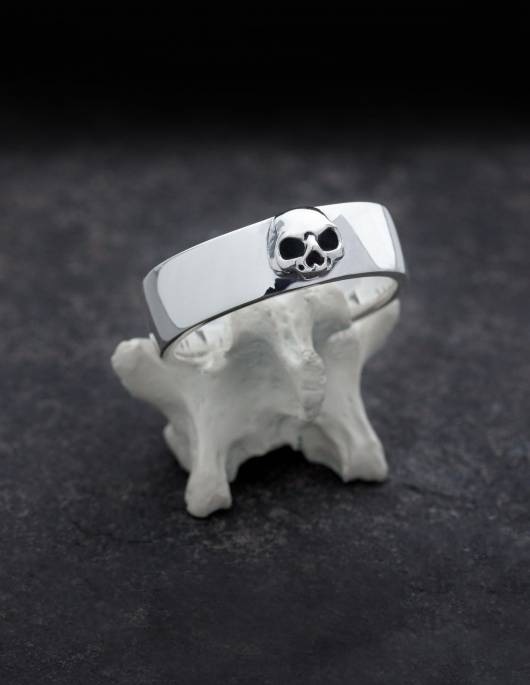 Amun is a simple band ring made of silver with a detailed skull without lower jaw. The ring has a flat shape that is very slightly curved on the inside and outside. It is presented standing on a bone.