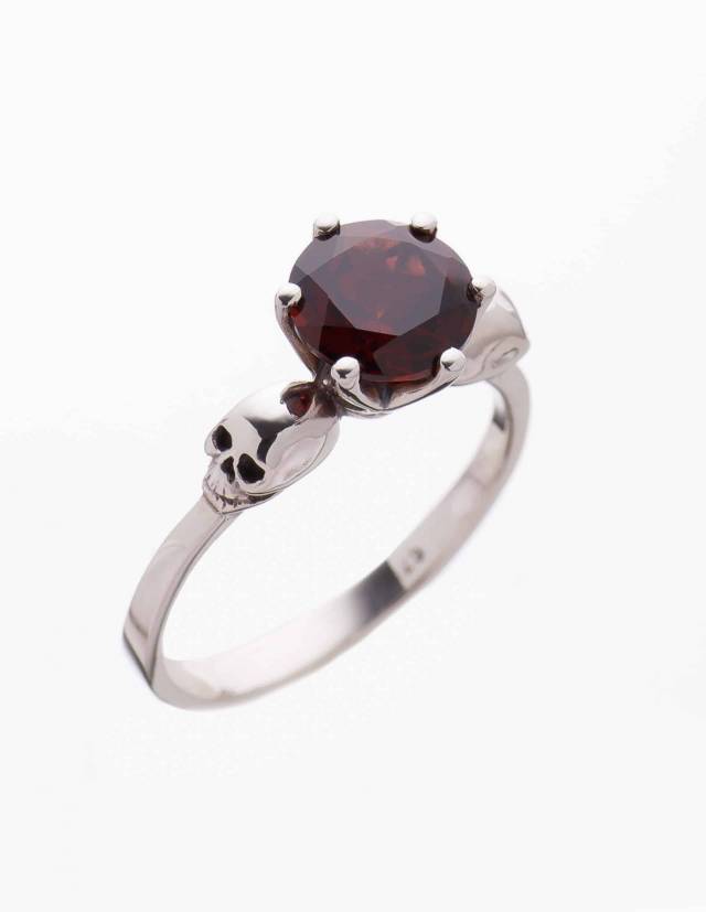 Detail of a dainty skull ring for women made of silver and 2ct garnet gemstone seen from above.