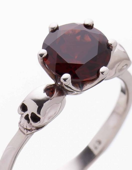 Detail of a dainty skull ring for women made of silver and garnet gemstone.