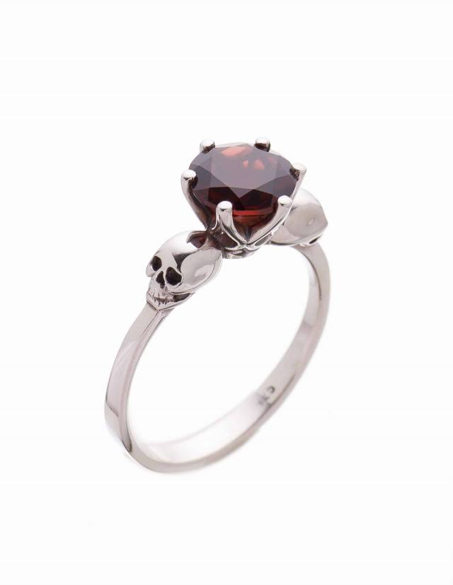 Detail of a dainty skull ring for women made of silver and a faceted garnet gemstone.