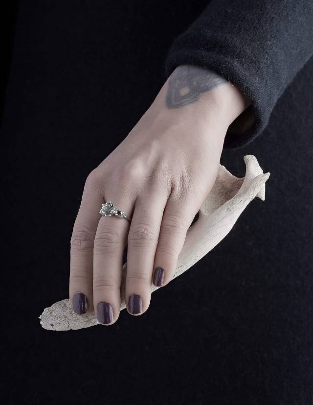Ein Kleiner Totenkopf Ring mit hellgrünem Edelstein aus Silber, gezeigt an einer Hand, die einen Knochen hält.