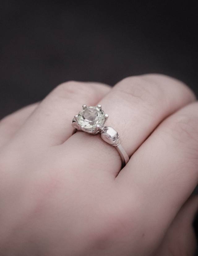 Ein Kleiner Totenkopf Ring mit hellgrünem Edelstein aus Silber, gezeigt an einer Hand aus der Nähe.