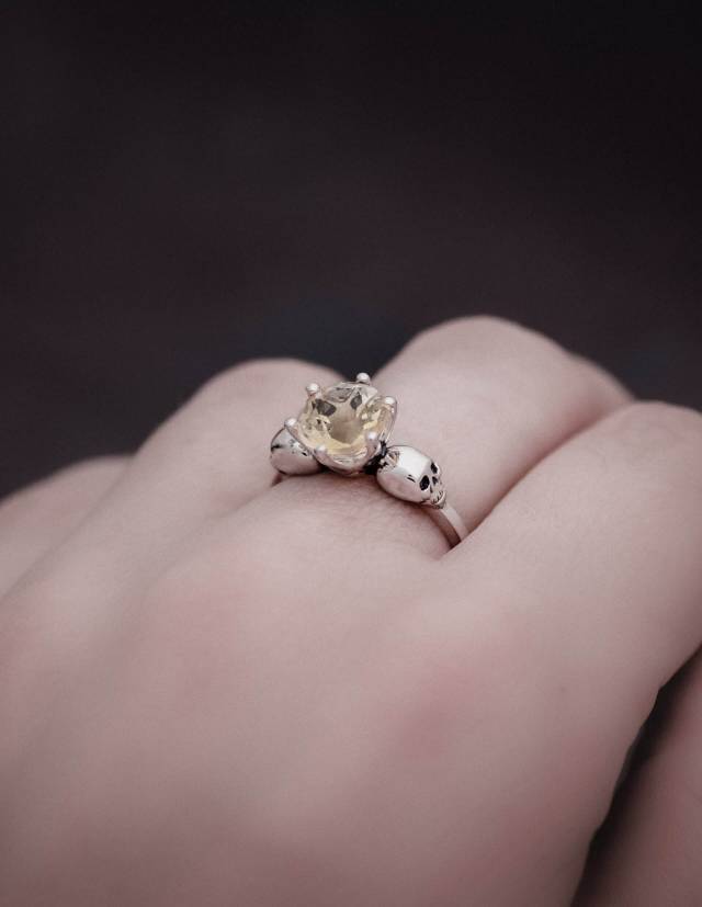 Skull irng made of silver with two little skulls and a light brown gemstone worn on a hand.