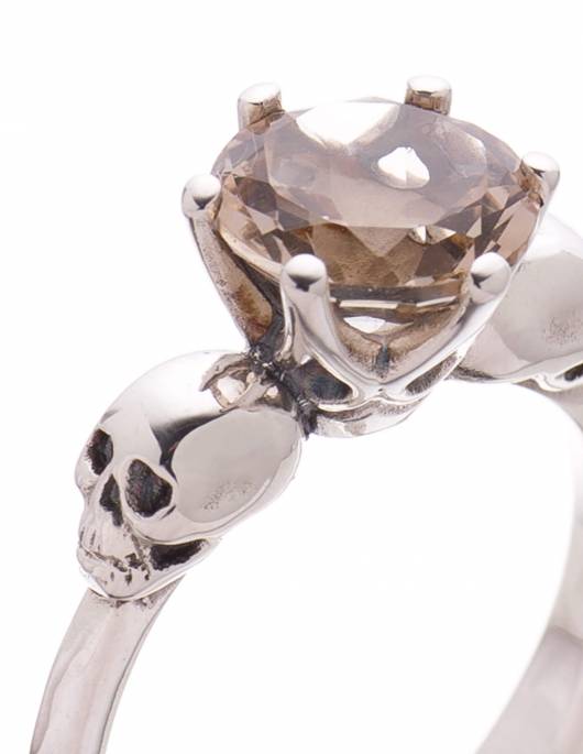 Detail of a dainty skull ring made of silver with two little skulls and a light brown smokey quartz gemstone.