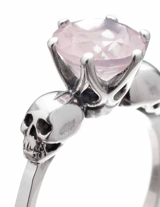 Detail of a tiny skull engagement ring with light pink stone shown on a hand. THe ring is named Wanda.