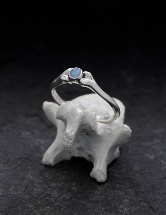 Ein kleiner Silberring mit einem hellblauen Opal steht auf einem Knochen.