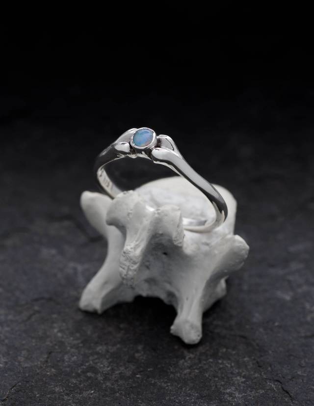 Une petite bague en argent avec une opale bleu clair est posée sur un os.