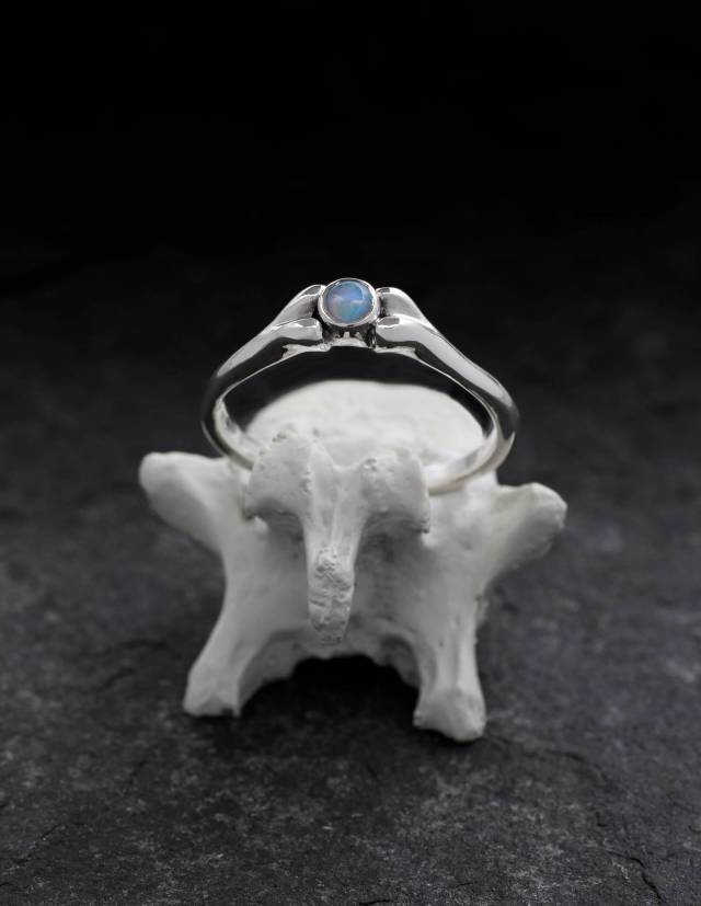 Une délicate bague en argent en forme d'os avec une pierre précieuse bleue.