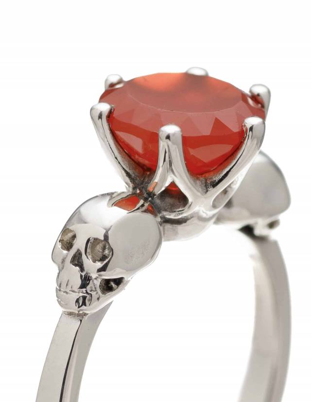Detail of a two skull ring with bright orange karnelian gemstone.