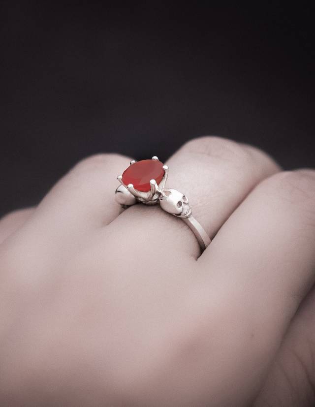 A two skull ring with bright orange karnelian gemstone worn on a womens hand.
