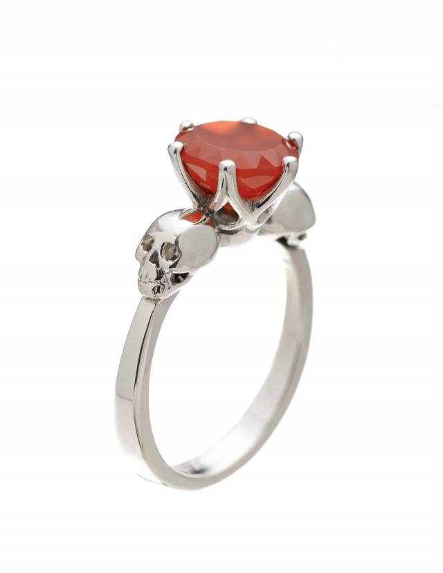 A dainty two skull ring with bright orange karnelian gemstone.