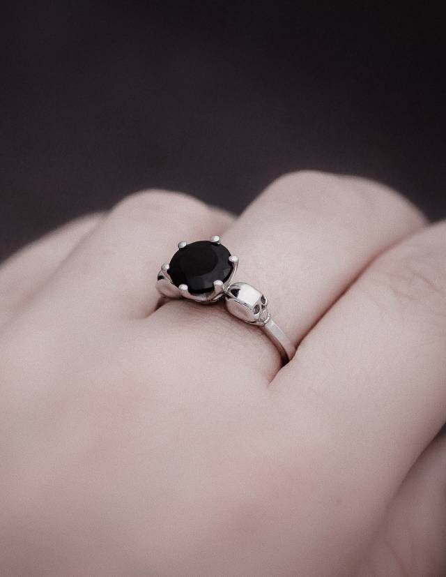 Close up of hand wearing a small sterling silver skull ring with black gemstone.