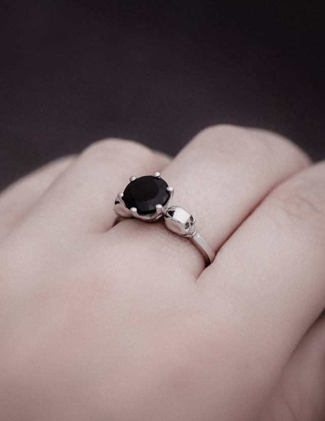 Vue rapprochée de la main portant une petite bague en argent sterling représentant un crâne avec une gemme noire.