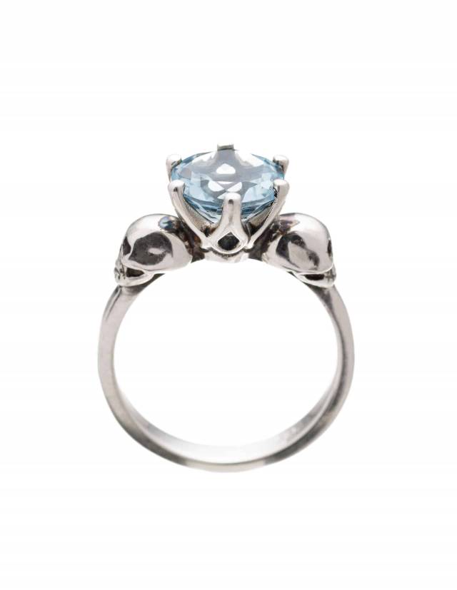 Pastel goth two skull ring with light blue topaz gemstone seen from the side.
