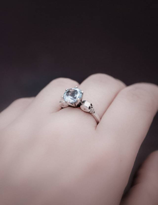 Pastel goth two skull ring with light blue topaz gemstone worn on a hand.