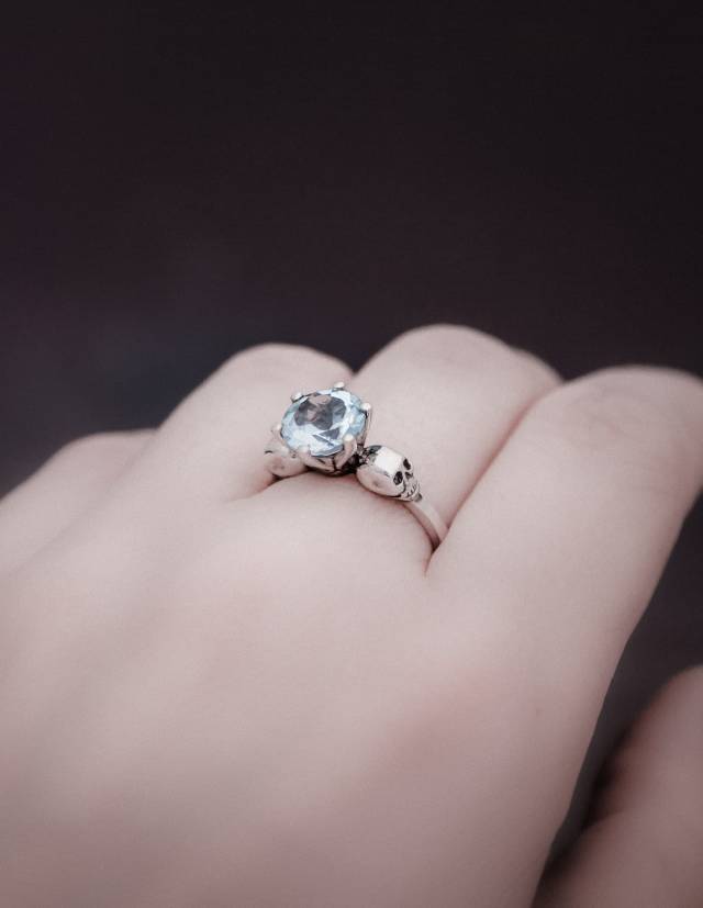 Anillo gótico de dos calaveras con gema de topacio azul claro que se lleva en una mano.