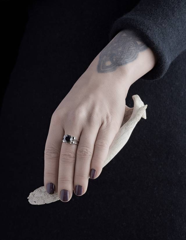 A sterling skull ring worn on a woman's hand holding a bone.