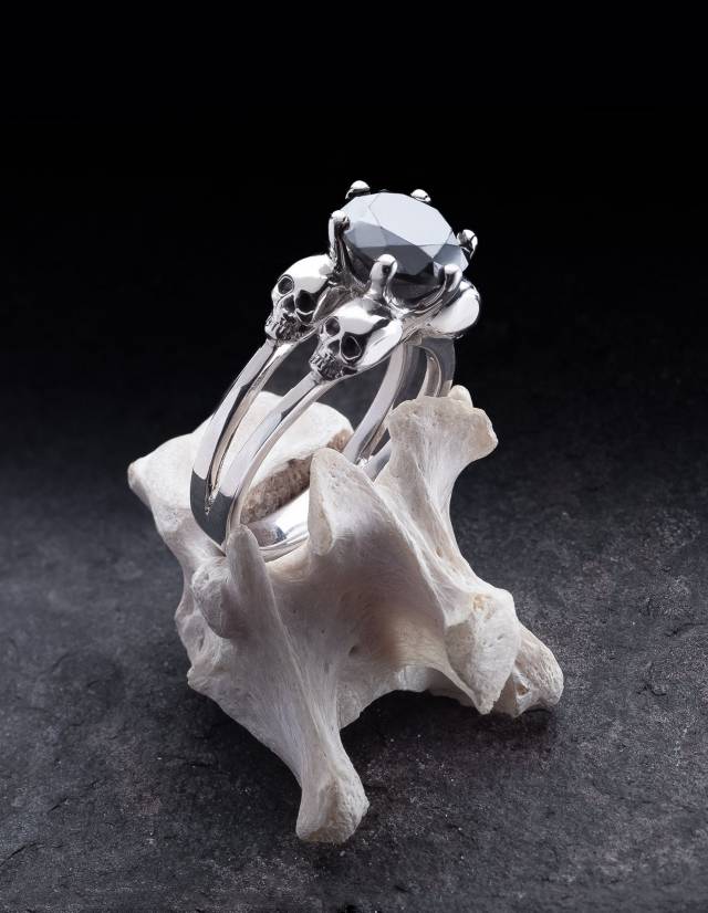 Ein Ring mit Skulls für Frauen aus Silber mirt einem schwarzen Edelstein wird auf einem Knochen präsentiert.