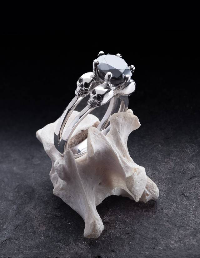 Se presenta un anillo con calaveras para mujer realizado en plata con una gema negra sobre un hueso.