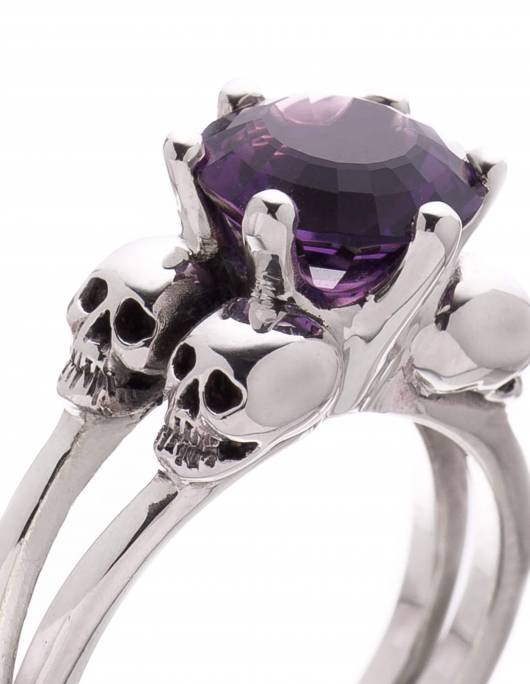 A skulll ring for women with 4 little skulls around a dark purple amethyst gemstone. The ring is named VARLA.