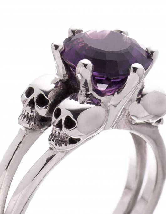 Anillo de calavera para mujer con 4 pequeñas calaveras alrededor de una gema amatista de color morado oscuro. El anillo se llama VARLA.