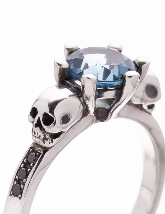 Une bague en forme de crâne dinosaure avec une gemme bleue et des diamants noirs dans la bande.