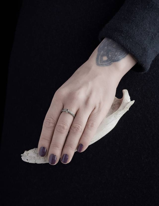 A dainty skull wedding rign made of silver worn on a hand holding a bone.