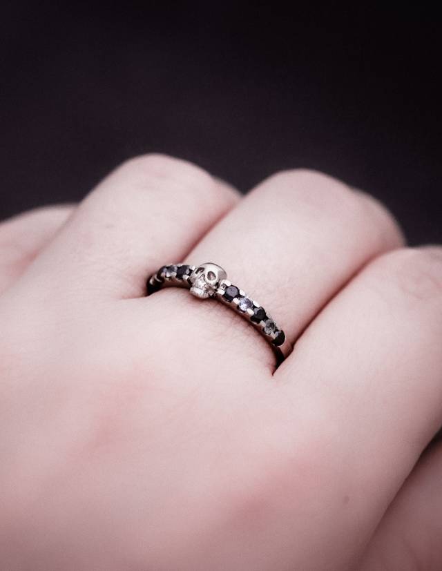 A dainty skull wedding rign made of silver worn on a hand.