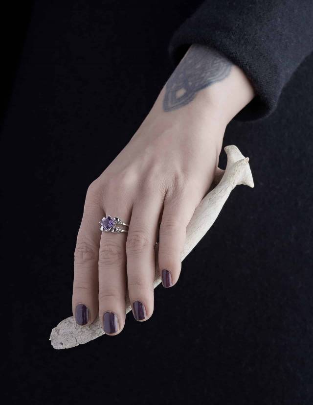 A silver engagement ring with 4 skulls for women with amethyst gemstone, shown on a hand...