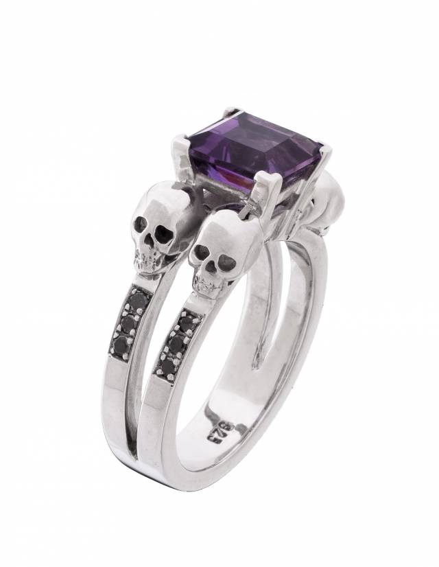 Elegant goth ring with 4 skulls and princess cut purpla amethyst gemstone, adorned with black diamonds on white background.