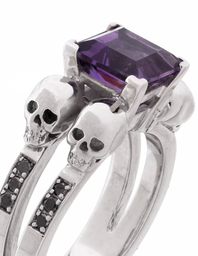 Elegant goth ring with 4 skulls and princess cut purpla amethyst gemstone, adorned with black diamonds, close up.
