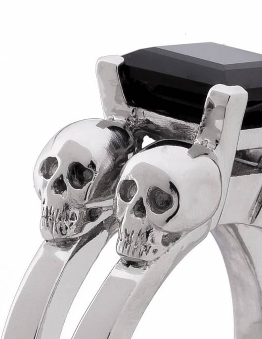 Goth ring for women made of sterling silver with little skulls and black gemstone, close up.