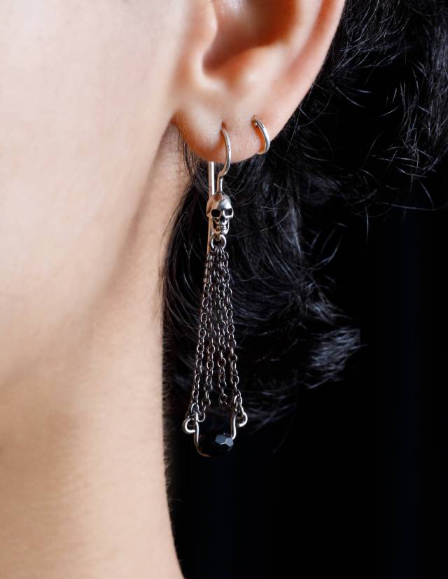 Goth earrings with a skull and black gemstone, worn.