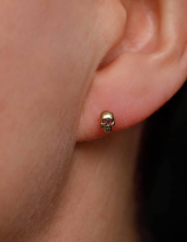 Detailed memento mori earrings in gold with ruby eyes.